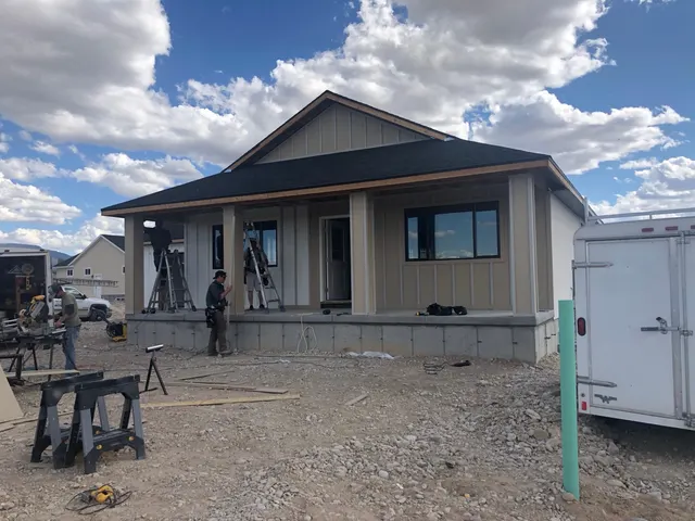 A house exterior with a covered front porch, ladders, tools, and people working on site.