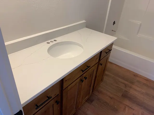 A wood bathroom vanity with dark handles, white veined countertop, and inset sink.