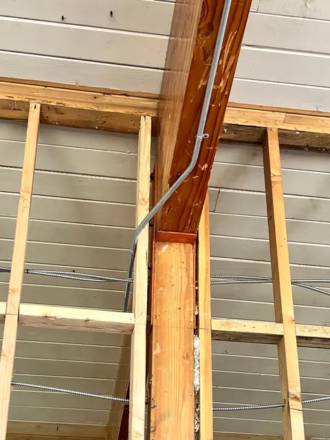 Metal electrical conduit follows a timber post and exposed wall framing.