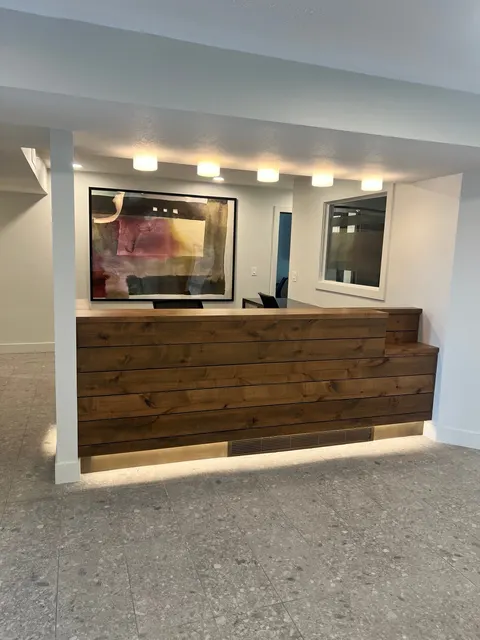 A wood-clad reception counter with under-counter lighting, overhead lights, and tiled floor.
