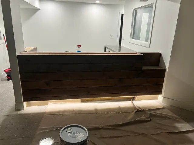 Wood-clad reception counter with under-counter lighting during finishing work.