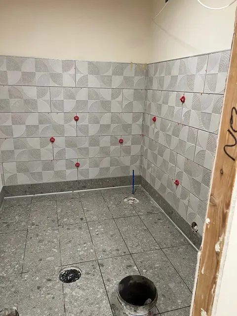 Patterned wall tiles and gray floor tiles with spacers and plumbing openings during installation.