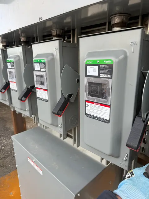 A close view of gray disconnect switches and conduit on the owner-described temporary power distribution assembly, with a gloved hand at lower right.